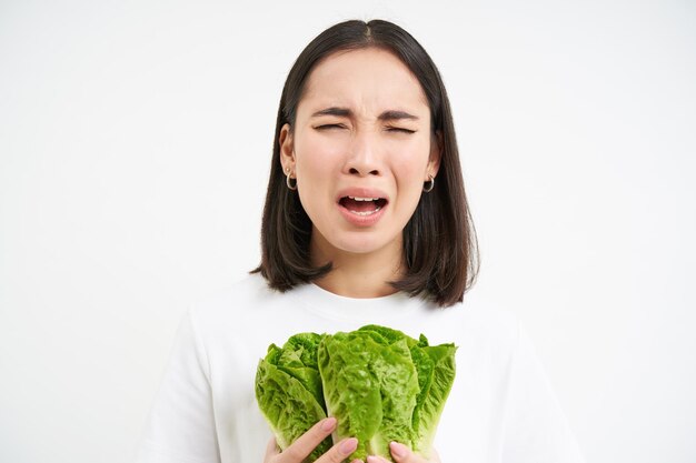 Kostenloses Foto gesunde ernährung und rohkost, traurige und unglückliche asiatische frau, die frische salatblätter und kohl in den händen hält