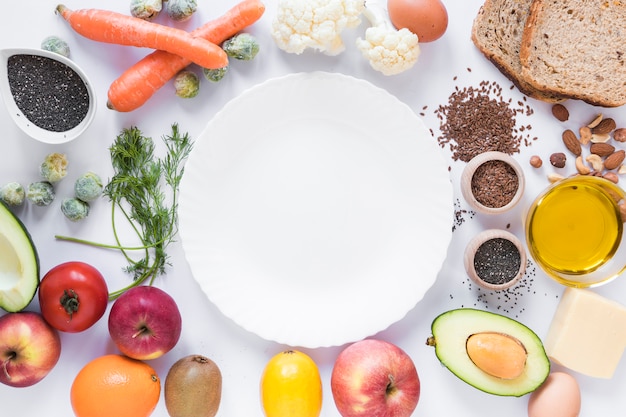 Gesunde Früchte; Gemüse; Trockenfrüchte; Brot; Samen und Käse; Ei; Öl; mit leerer Platte über weißem Hintergrund