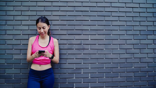 Gesunde schöne junge asiatische Athletenfrau, die Smartphone für die Prüfung des Social Media verwendet