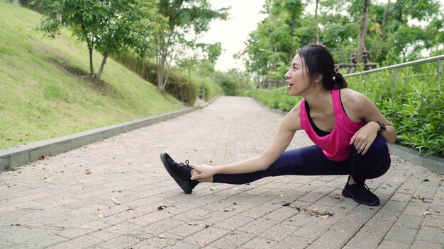 Gesunde schöne junge asiatische Athletenfrauen in den Sportkleidungsbeinen, die ihre Arme wärmen und ausdehnen