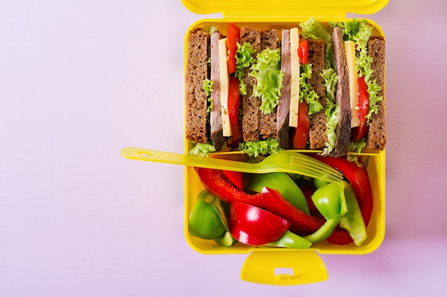 Gesunde Schul-Brotdose mit Rindfleischsandwich und frischem Gemüse auf rosa Tisch. Draufsicht. Flach liegen