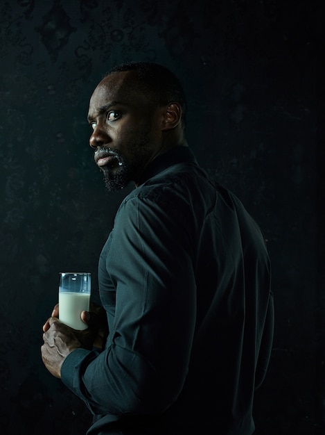 Gesunder junger afrikanischer Mann, der Tasse Milch auf einem schwarzen Studiohintergrund hält.