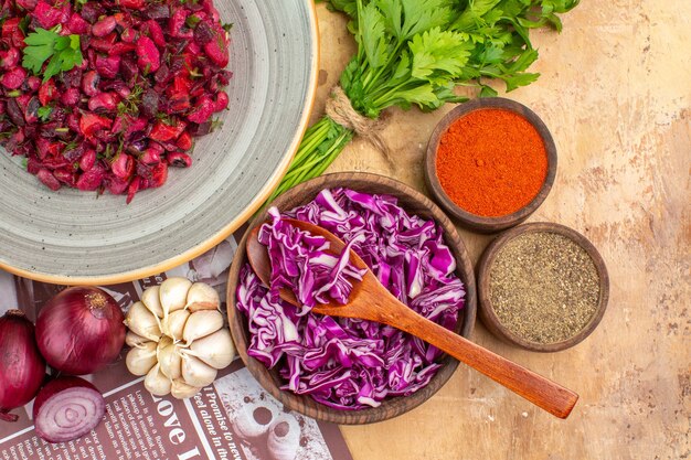 Gesunder Rote-Bete-Salat von oben auf einer grauen Keramikplatte mit roten Zwiebeln, Knoblauch und Petersilie und einer Schüssel mit schwarzem Pfeffer, Kurkuma, gemahlenem Pfeffer, Rotkohl auf einem Holztisch