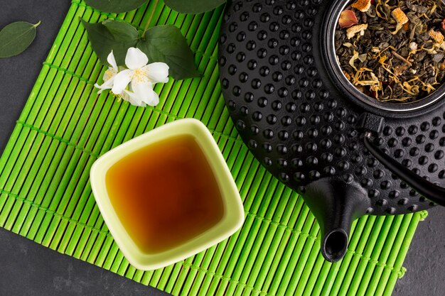 Gesunder Tee in der keramischen Schüssel mit trockenen Blättern auf grüner Platzmatte