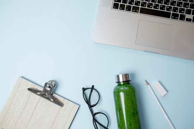 Gesundes Arbeitsleben Laptop mit Schreibwaren und grünen Smoothies mit Apfel auf blauem Tisch Draufsicht flach gelegt