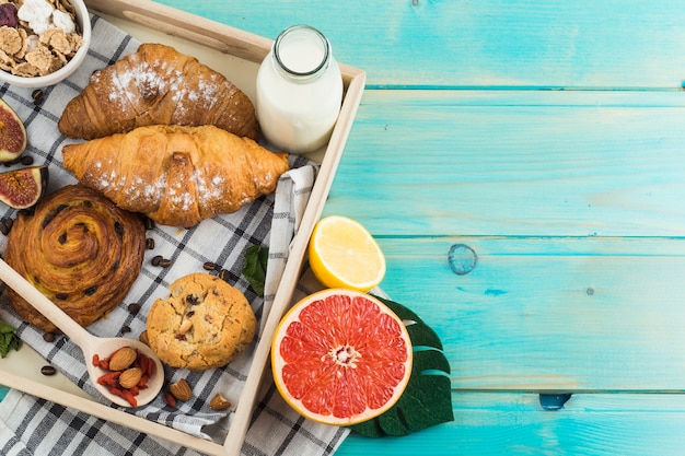 Kostenloses Foto gesundes frühstück mit croissant; gesicherte kekse; milch; müsli; und zitrusfrüchte auf holztablett