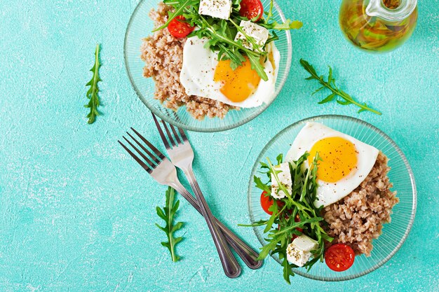 Gesundes Frühstück mit Ei, Feta, Rucola, Tomaten und Buchweizenbrei auf hellem Hintergrund. Richtige Ernährung. Diätmenü. Flach liegen. Ansicht von oben