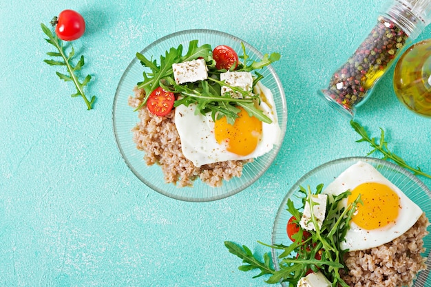 Gesundes Frühstück mit Ei, Feta, Rucola, Tomaten und Buchweizenbrei auf hellem Hintergrund. Richtige Ernährung. Diätmenü. Flach liegen. Ansicht von oben