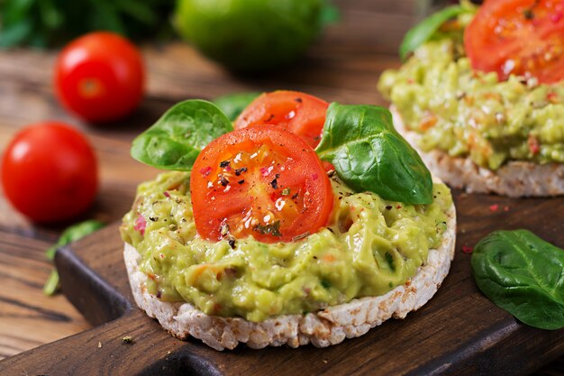 Gesundes Frühstück. Sandwich Knäckebrot mit Guacamole und Tomaten auf einem Holztisch.