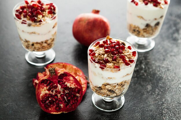 Gesundes hausgemachtes Dessert aus Müsli, Joghurt und Granatapfel auf dunklem Holzhintergrund