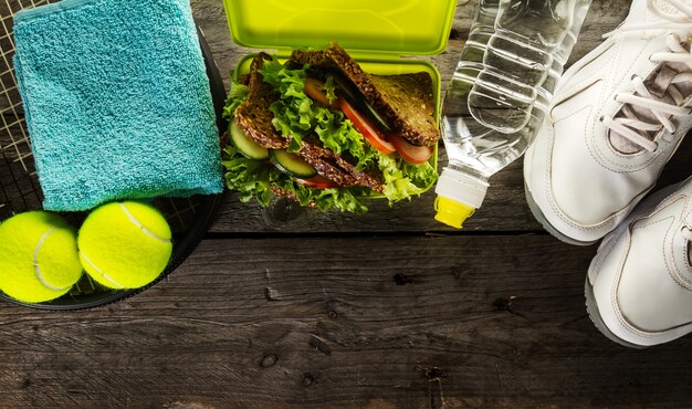 Gesundes Leben Sport Konzept. Sneakers mit Lunchbox, Handtuch und Flasche Wasser auf hölzernem Hintergrund. Text kopieren