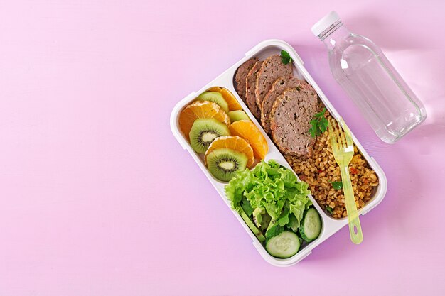 Gesundes Mittagessen mit Bulgur, Fleisch und frischem Gemüse und Obst auf einer rosa Oberfläche. Eignung und gesundes Lebensstilkonzept. Brotdose. Ansicht von oben