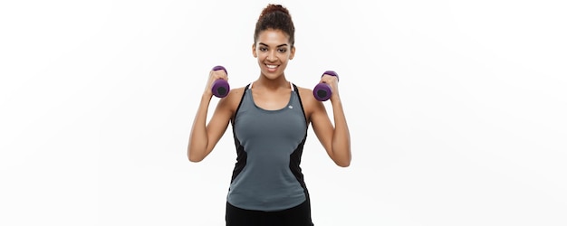 Gesundes und Fitness-Konzept Schöne amerikanisch-afrikanische Dame im Fitness-Kleidungstraining mit Hantel isoliert auf weißem Hintergrund
