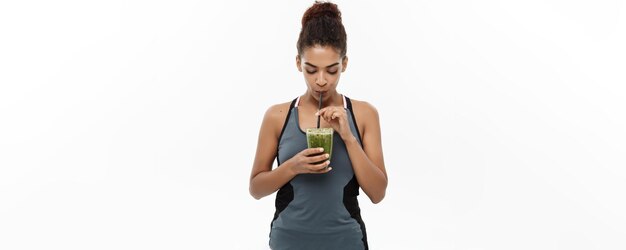 Gesundes und Fitness-Konzept Schöne amerikanisch-afrikanische Dame in Fitnesskleidung trinkt gesundes Gemüsegetränk isoliert auf weißem Hintergrund