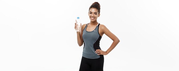Gesundes und Fitness-Konzept Schönes afroamerikanisches Mädchen in Sportkleidung mit Plastikwasserflasche nach dem Training isoliert auf weißem Studiohintergrund