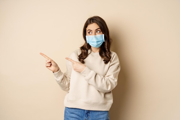 Gesundheits- und Covid-Konzept süße brünette Frau in medizinischer Gesichtsmaske, die mit dem Finger nach links auf Logo-Banner zeigt ...