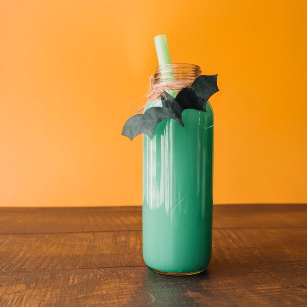 Getränk der grünen Farbe in der Flasche mit handgemachtem Schläger auf orange Hintergrund