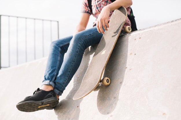 Getreidejugendlicher mit dem Skateboard, das auf Rampe sitzt