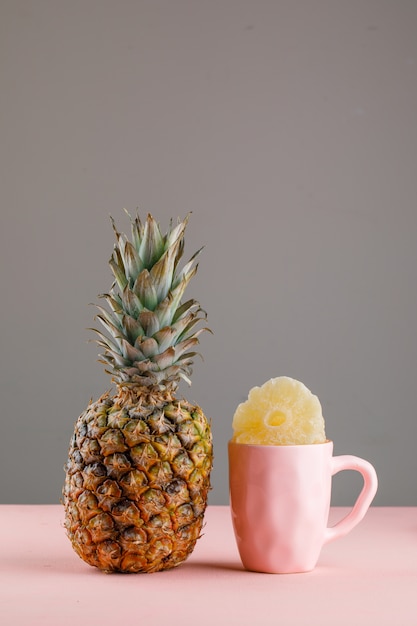 Getrocknete Ananas in einer Tasse mit frischer Ananas auf rosa und grauer Oberfläche