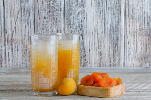 Getrocknete Aprikosen in einem Holzteller mit Saft, frische Aprikosenseitenansicht auf einem Holztisch