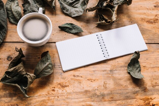 Getrocknete Blätter, Tasse Kaffee und Notizbuch auf hölzernem Hintergrund