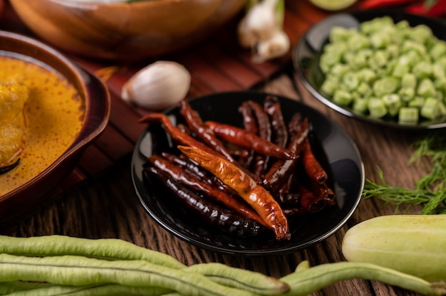 Getrocknete Chilis in einem schwarzen Teller mit Linsen gebraten. Gurken und Knoblauch werden auf den Holztisch gelegt