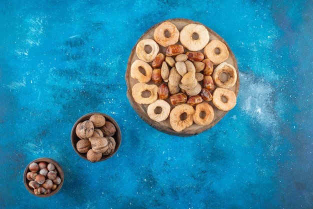 Getrocknete früchte und leckere nüsse auf einem brett, auf dem blauen tisch.