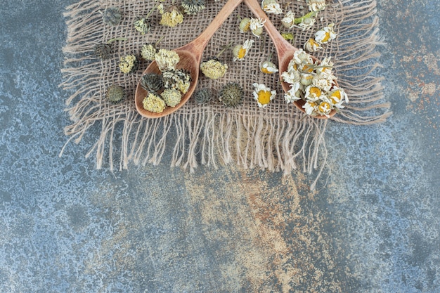 Getrocknete Kamille und andere Blumen auf Sackleinen mit Holzlöffeln.