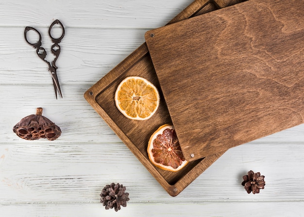 Getrocknete Orange; Grapefruitscheibe; Lotus-Hülse; Tannenzapfen mit einer Schere auf einem weißen Holztisch