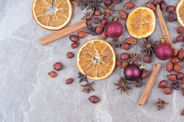 Getrocknete Orange mit Weihnachtskugeln und Hagebutten auf Steinoberfläche.