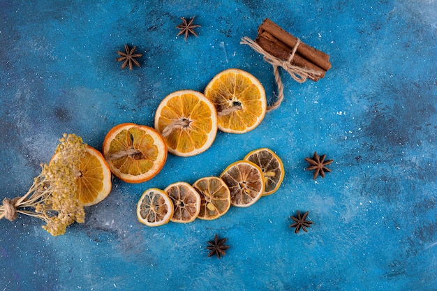 Getrocknete Orangenscheiben mit Zimtstangen auf blauem Tisch.