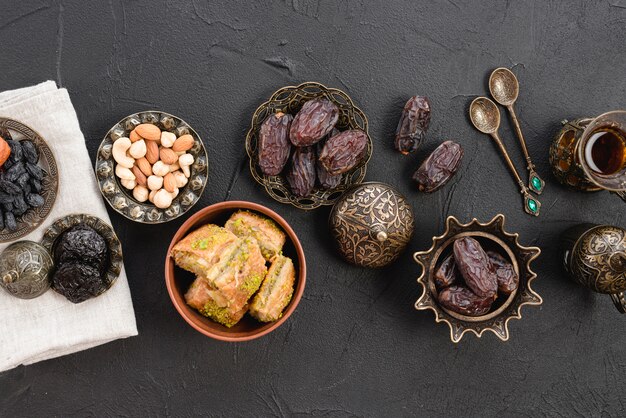 Getrocknete rohe Bio-Datteln; Nüsse und Baklava auf metallischer Eisenplatte über dem schwarzen Hintergrund
