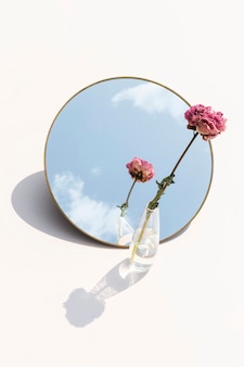 Getrocknete rosa pfingstrose in einer klaren vase, die auf einem spiegel reflektiert wird