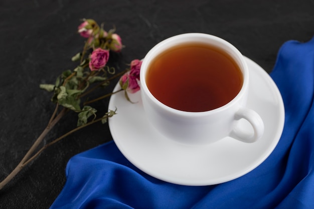 Getrocknete Rosen mit einer Tasse heißem Tee auf einem schwarzen Tisch.