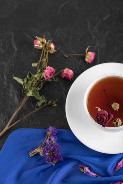 Getrocknete Rosen mit einer Tasse heißem Tee auf einem schwarzen Tisch.