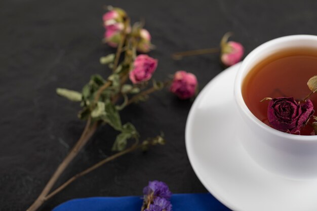 Getrocknete Rosen mit einer Tasse heißem Tee auf einem schwarzen Tisch.