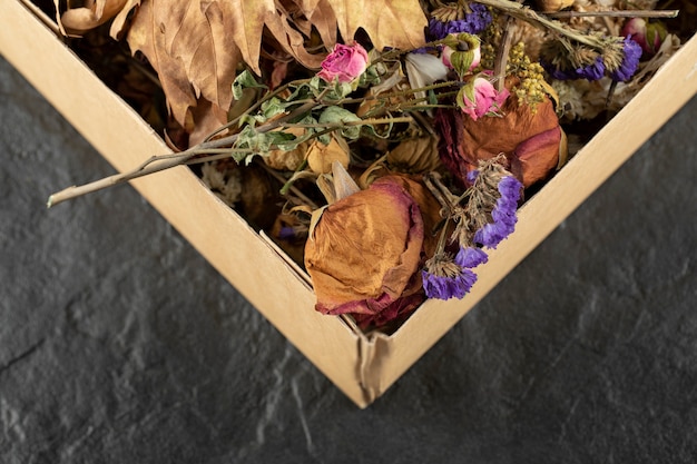 Getrocknete Rosenblüten mit getrockneten Blättern in einer Pappschachtel.