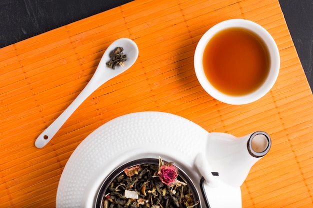 Getrocknetes Teekraut und Tee auf Platzmatte mit keramischer Teekanne