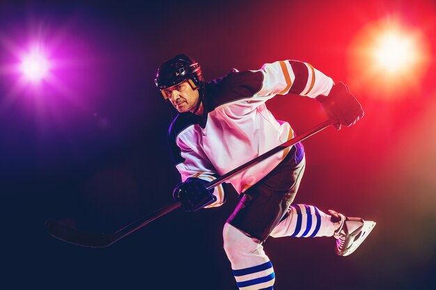 Gewinner. Männlicher Hockeyspieler mit dem Stock auf dem Eisplatz und der dunklen neonfarbenen Wand Sportler mit Ausrüstung, Helmübungen. Konzept des Sports, des gesunden Lebensstils, der Bewegung, des Wellness, der Aktion.