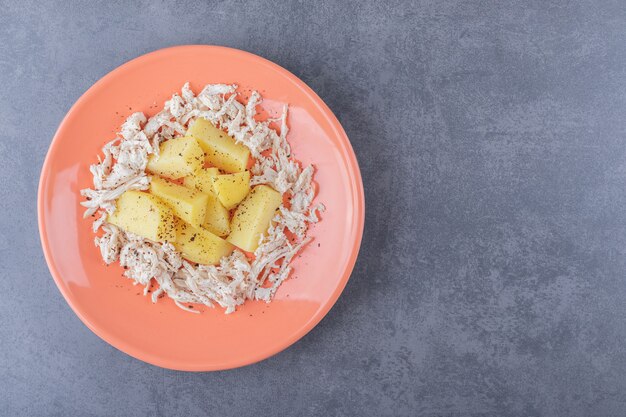 Gewürfeltes Huhn mit Salzkartoffeln auf orangefarbenem Teller.