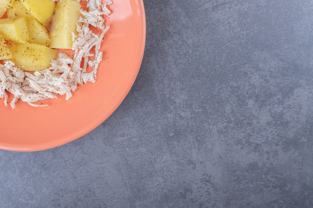 Gewürfeltes Huhn mit Salzkartoffeln auf orangefarbenem Teller.