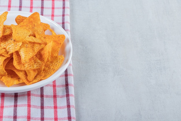 Gewürzte Dreieckschips auf weißer Platte auf Stein.