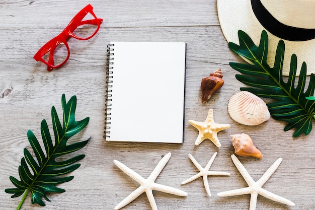 Gewundenes Notizbuch mit Muschel, Blatt, Strohhut, Sonnenbrille und Starfish auf Tabelle