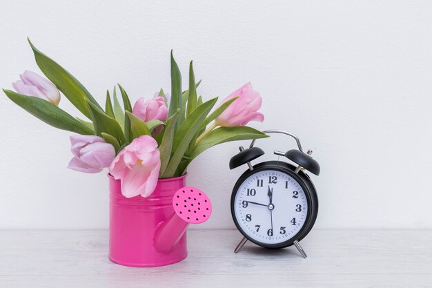Gießkanne mit Blumen und Uhr
