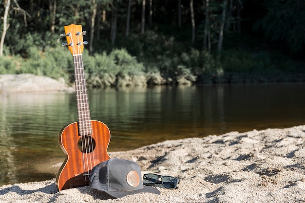 Gitarre mit Mütze und Sonnenbrille am Ufer in der Nähe von Wasser