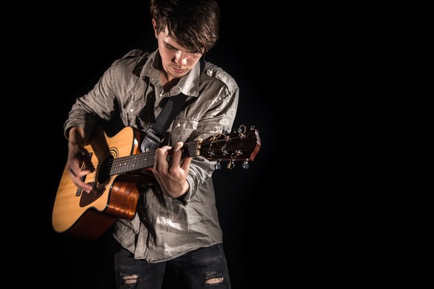 Gitarrist, Musik. Ein junger Mann spielt eine Akustikgitarre auf einem schwarzen isolierten Hintergrund. Spitzlicht