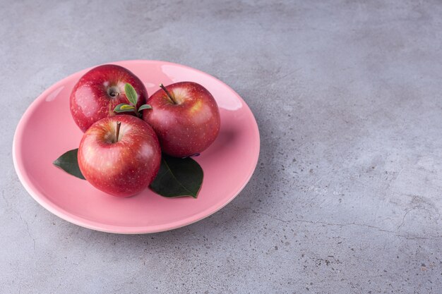 Glänzend rote Äpfel mit grünen Blättern auf Stein.