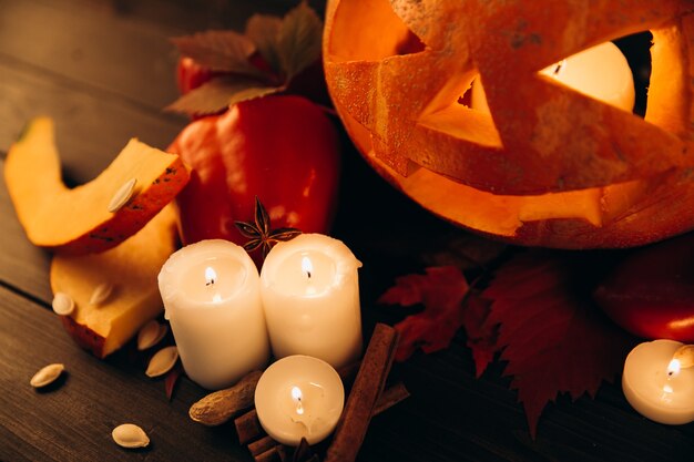Glänzende Kerzen, Zimt und abgefallene Blätter stehen vor Halloween Kürbis