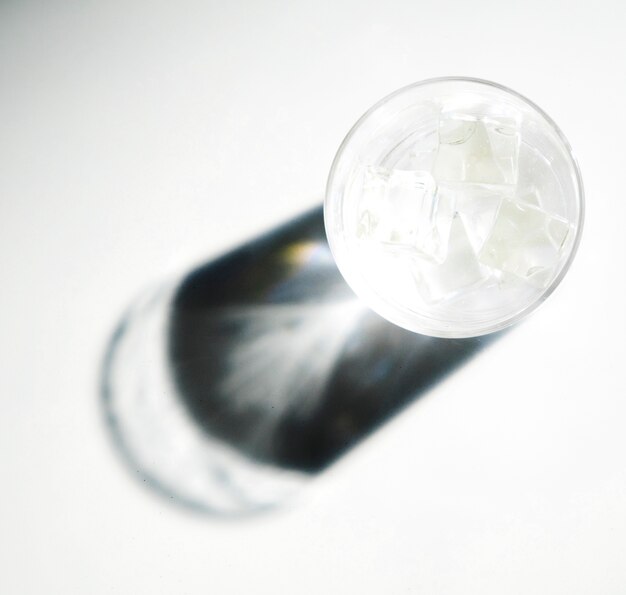 Glänzendes Sonnenlicht auf dem dunklen Schatten des Glases mit Eiswürfeln auf weißem Hintergrund