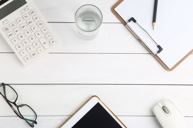 Gläser, Taschenrechner und Tablette auf weissem Schreibtisch